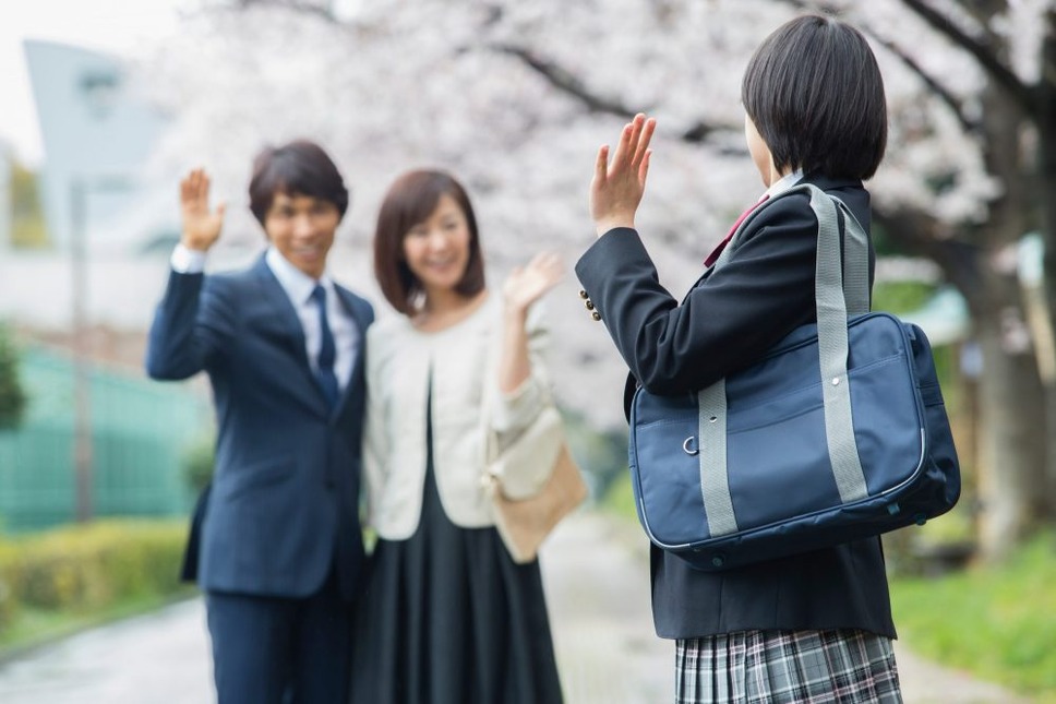 桜の下で両親に手を振る女子高生