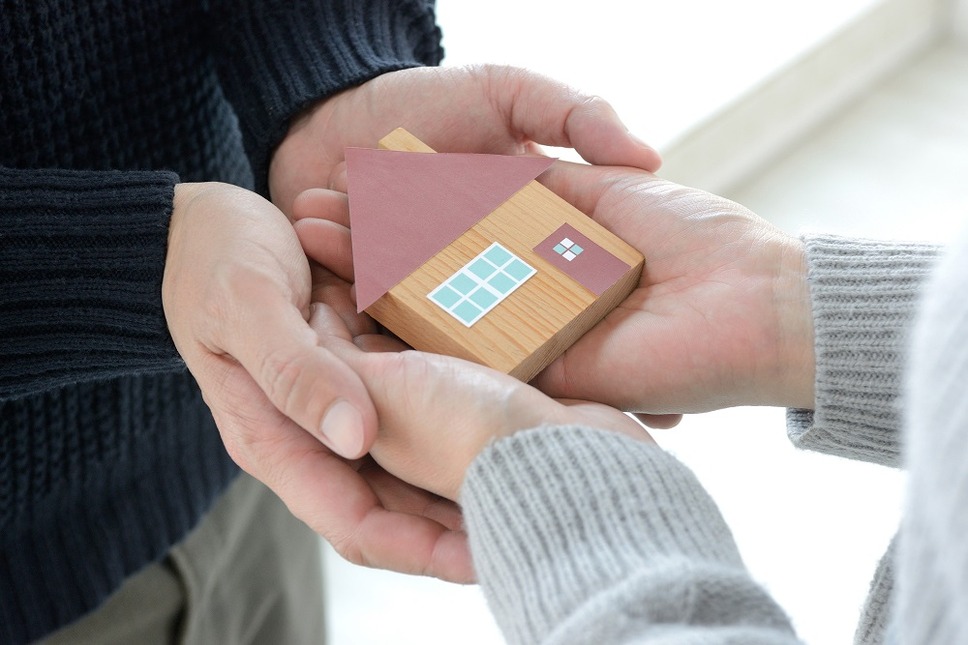 男性と女性の手に包まれた住宅模型